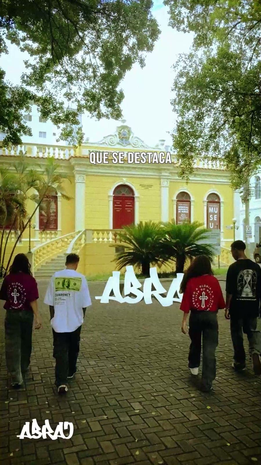 Jovens com camisetas da Abraj caminhando diante de um prédio amarelo, com o logo da marca no canto